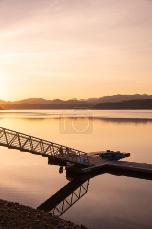 Téléchargez les photos : Scenic view of pier on lake with mountains silhouette background, sunset time - en image libre de droit
