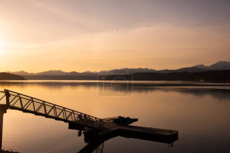 Foto de Scenic view of pier on lake with mountains silhouette background, sunset time - Imagen libre de derechos