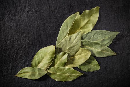 Foto de Un montón de hojas de laurel secas sobre un fondo negro. Laurel aromático de especias. Receta ingredientes. - Imagen libre de derechos