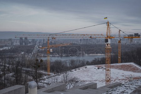 Téléchargez les photos : Kiev, Ukraine. Le 28 novembre 2023, la construction avec des grues de construction se poursuit près du Dnipro. Une belle vue sur la ville d'en haut - en image libre de droit