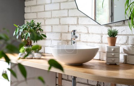 Foto de Elegante interior de baño moderno con lavabo de cerámica en el mostrador de madera y espejo en la pared de ladrillo blanco. - Imagen libre de derechos