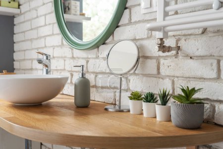 Photo for Industrial interior of bathroom with window, wooden furniture and counter with ceramic sink and round mirror on white brick wall. Modern design at home. - Royalty Free Image