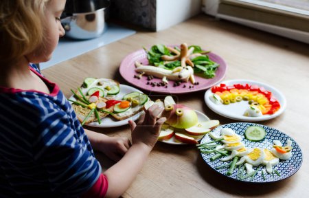 Foto de Niña comiendo comida colorida y verduras y frutas saludables en diferentes formas. Diversión con la comida para niños por la mañana. Desayuno divertido para niños. - Imagen libre de derechos