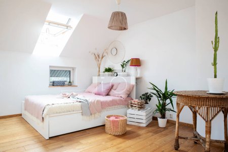 Photo for Cozy bedroom in white and pink color with comfortable bed and pink pillow. Scandinavian interior in apartment in the attic with stylish decoration and wooden floor. - Royalty Free Image