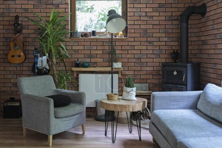 Photo for Design room in a rural cottage with comfortable sofa and armchair, red brick wall, fireplace and wooden stylish table. Cozy interior with stylish decor. - Royalty Free Image