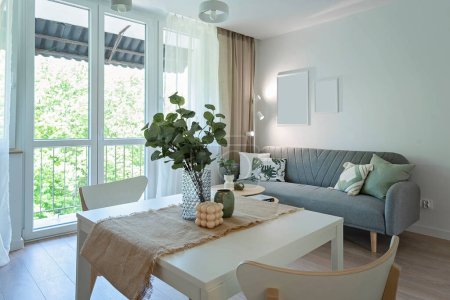 Foto de Interior del comedor con ventana con cortinas, sofá con almohada y mesa con sillas. Habitación con marco vacío en la pared en el apartamento. - Imagen libre de derechos