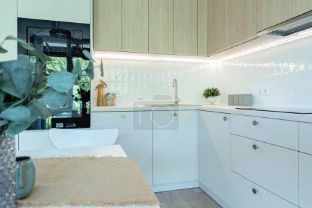 Foto de Lujosa cocina con muebles blancos con armarios y cajones y horno. Interior moderno con comedor con elegante diseño dorado. - Imagen libre de derechos