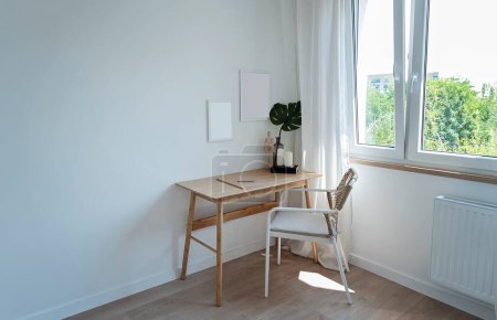 Foto de Minimalismo en la sala de oficina con mesa de oficina de madera y silla cerca de la ventana. Espacio para trabajar con marco vacío en la pared. Interior de la habitación en apartamento nuevo. - Imagen libre de derechos