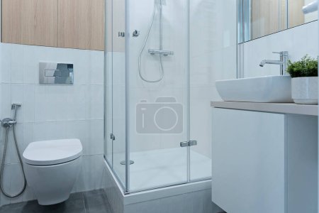 Téléchargez les photos : Intérieur de salle de bain minimaliste avec carrelage blanc, toilettes, douche, lavabo en céramique avec robinet sur l'armoire. Architecture intérieure. - en image libre de droit