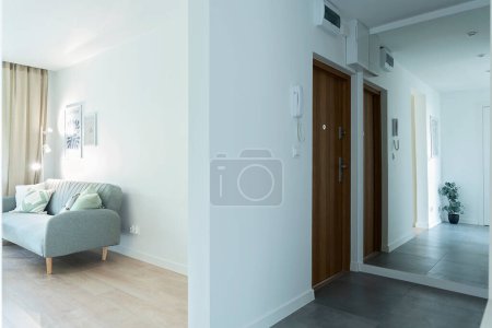Foto de Interior del pasillo y pasillo con puerta, espejo y paredes blancas. Apartamento nuevo con parquet de madera y sofá de diseño. Espacio abierto. Propiedad. - Imagen libre de derechos