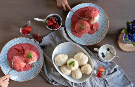 Photo for Homemade and healthy meal for children on a table. Sweet strawberry sauce with boild steamed dumplings on a plate with hand. Food i restaurant. Top view. - Royalty Free Image