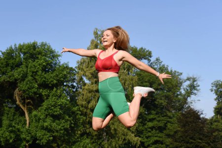 Foto de Deportiva salta y vuela durante el entrenamiento y practica ejercicio. Energía, actividad y fuerza en el cuerpo deportivo. Mujer feliz en estilo de vida saludable al aire libre. - Imagen libre de derechos