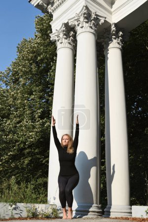 Photo for Standing woman in yoga position and practicing meditation and body balance outdoors in park. Vertical. Healthy lifestyle. - Royalty Free Image
