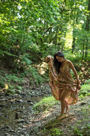 Photo for Woman walking barefoot in long dress in a forest among green. Relax with nature and happy summer. Vertical. - Royalty Free Image