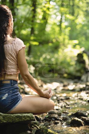 Photo for Young fitness woman practicing and meditate in lotus pose among nature. Yoga morning routine with gyan mudra. Healthy lifestyle. - Royalty Free Image