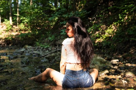 Téléchargez les photos : Femme avec les cheveux longs assis dans une rivière et se détendre. Pratiquer la méditation et l'exercice calme du yoga. Nature en plein air. - en image libre de droit