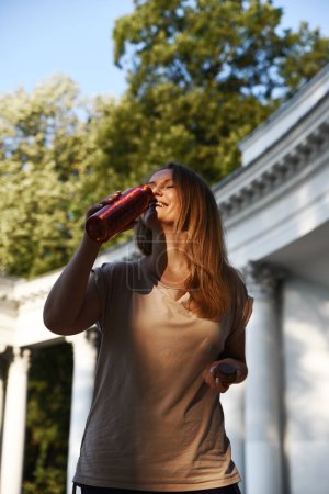 Téléchargez les photos : Femme sportive buvant femme de bouteille d'eau après le jogging et la formation. Pause dans le sport. Style de vie sain à l'extérieur. - en image libre de droit