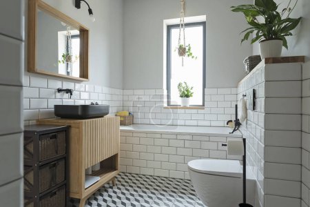 Foto de Acogedor cuarto de baño en el interior de estilo en el nuevo apartamento con azulejos de textura en el suelo y baldosas blancas en la pared. Gabinete de madera debajo del lavabo y espejo de diseño. - Imagen libre de derechos
