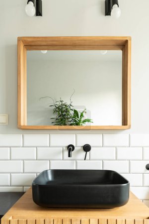 Photo for Ceramic black basin on wooden cabinet in industrial bathroom in loft apartment. Stylish interior with square mirror on white tiles on the wall. - Royalty Free Image