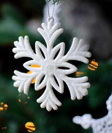 Foto de Copo de nieve blanco colgando de una rama verde de abeto como decoración navideña con luces bokeh. Diciembre, invierno y vacaciones. Vertical - Imagen libre de derechos
