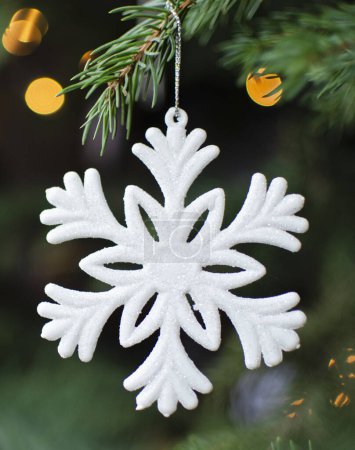 Foto de Copo de nieve blanco colgando de una rama verde de abeto como decoración navideña con luces bokeh. Diciembre, invierno y vacaciones. Vertical. - Imagen libre de derechos