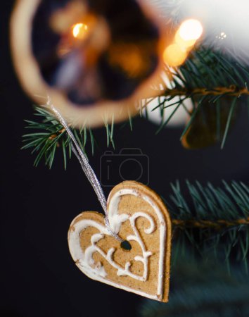 Foto de Dulce decoración de Navidad corazón de jengibre colgando de una rama con luces. Vacaciones y tarjeta de Navidad. Vertical. Navidad.. - Imagen libre de derechos