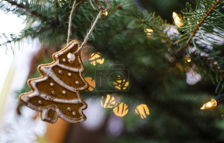 Téléchargez les photos : Carte de Noël avec espace de copie. Pain d'épice décoratif suspendu au sapin de Noël vert avec des lumières de fées avec bokeh. - en image libre de droit