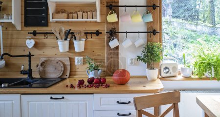 Vintage rustikale Küche mit weißen Holzmöbeln, Holzwand und rustikalem Dekor. Vintage-Geschirr und Detalis. Preiselbeere und Kürbis auf dem Borad. Licht drinnen..