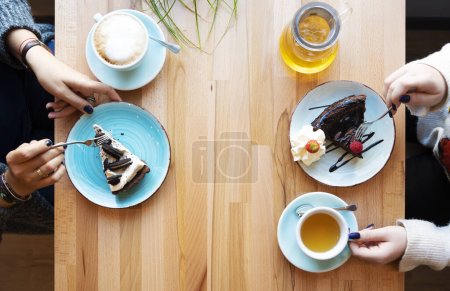 Photo for Pieces of cake on a plate and cup of cooffee and tea. Woman's hand holds a cup. Wooden table with copy space. Sweet food. - Royalty Free Image