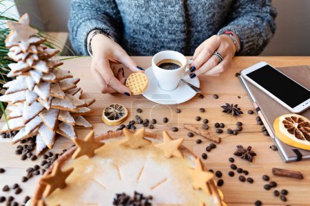 Téléchargez les photos : Tasse de café avec gâteau de Noël sur une table en bois au restaurant. Mains de femme avec expresso, téléphone et café aux haricots pendant les vacances de pause. Temps de Noël et fermer. - en image libre de droit