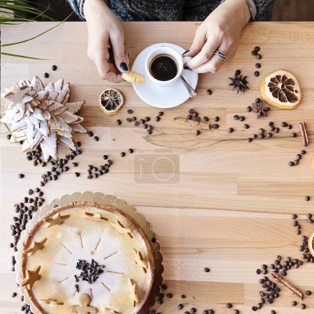 Foto de Taza de café expreso con canela y frijoles sobre una mesa de madera con espacio para copiar. Las manos de la mujer sostienen una taza alrededor de la decoración de Navidad. Pastel casero y feliz navidad de confitería. - Imagen libre de derechos