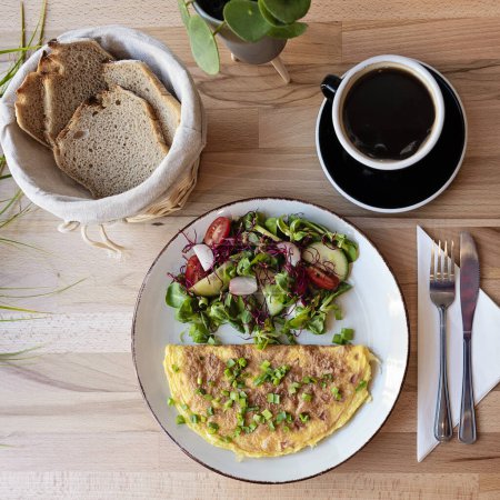 Téléchargez les photos : Omelette avec salade dans une assiette avec café noir pour le petit déjeuner sur une table en bois au restaurant. Nourriture végétarienne savoureuse. - en image libre de droit