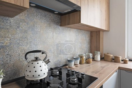 Photo for Kitchen with wooden counter, stove with gas and kettle, modern pattern tiles on the wall. Stylish interior of design kitchen in apartment. - Royalty Free Image