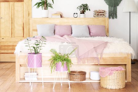 Téléchargez les photos : Boho intérieur de chambre avec meubles en bois et lit avec couverture rose et oreillers et plantes. Plancher en bois dans le chalet. Maison confortable. - en image libre de droit