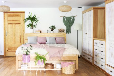 Photo for Boho interior of bedroom with wooden furniture and bed with pink blanket and pillows and plants. Wooden floor in the cottage. Comfortable home. - Royalty Free Image