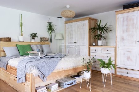 Foto de Interior boho de dormitorio con muebles de madera y cama con almohadas grises y plantas. Suelo de madera en la cabaña. Cómodo hogar. - Imagen libre de derechos