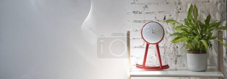 Photo for Design red clock and green plant on the shelf on the white wall with bricks. Blank place for text with copy space. Panoramic banner. - Royalty Free Image