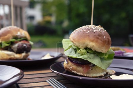 Photo for Hamburger on a plate. Homemade burger with meat and lettuce on a table in a garden during barbeque and grill. Outdoor lunch or dinner. Close up. - Royalty Free Image