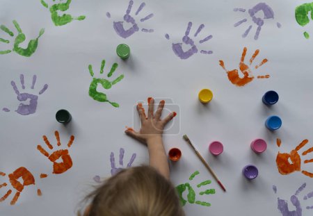 Téléchargez les photos : Enfant peint les mains sur un fond blanc. Empreinte colorée et empreinte de main comme un concept pour le plaisir, le jeu sensoriel et la créativité en kidergarten. Éducation. - en image libre de droit