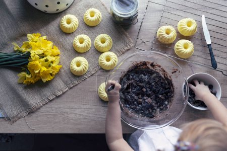 Téléchargez les photos : Petite fille faisant des muffins faits maison avec du chocolat. Boulangerie à la maison dans la cuisine avec une délicieuse recette de dessert sain. Mains d'enfant avec cuillère. Vue du dessus. - en image libre de droit