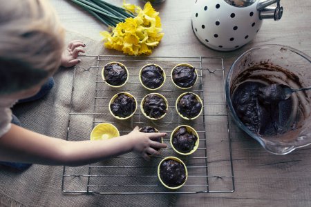 Téléchargez les photos : Petite fille faisant des muffins faits maison avec du chocolat. Boulangerie à la maison dans la cuisine avec une délicieuse recette de dessert sain. Mains d'enfant. Vue du dessus. - en image libre de droit
