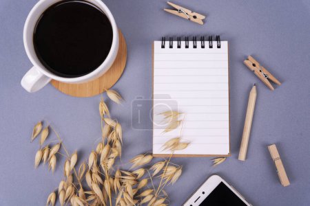 Photo for Empty notebook with mock up, cup of coffee, wooden clip, pencil , clock and smartphone on grey office desk. Table top for business and planning. Flat lay. - Royalty Free Image