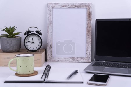 Téléchargez les photos : Bureau blanc avec cadre vierge pour écrire, café, horloge et ordinateur portable pour le travail. Affaires et technologie au bureau à domicile. - en image libre de droit