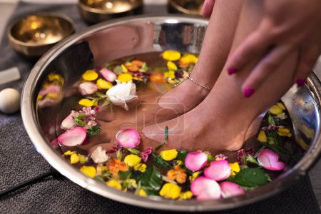 Téléchargez les photos : Massage des pieds et thérapie des pieds dans un salon de spa dans un bol rempli de pentaux de fleurs et de roses. Pédicure et aromathérapie. Gros plan. - en image libre de droit