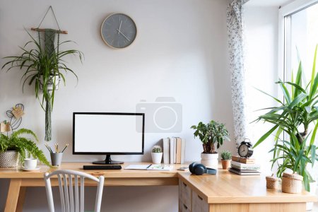 Photo for Blank screen of monitor in computer on wooden office desk in stylish business room with white wall and mock up. Light interior of office space with plants and laptop in vintage style. - Royalty Free Image