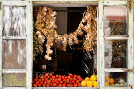 Foto de Pimientos rojos frescos y ajo colgante en el mostrador en la ventana en la tienda de comestibles. Hortalizas saludables. - Imagen libre de derechos