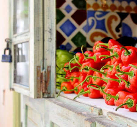 Téléchargez les photos : Empilement de poivrons rouges à vendre sur le comptoir en bois dans la fenêtre du marchand de légumes. Légumes crus sains. - en image libre de droit