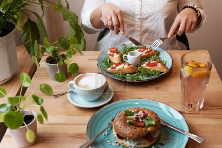 Foto de Comida vegetariana en un plato con café en el almuerzo en el restaurante. Las manos de las mujeres con cubiertos comen una comida saludable para el desayuno. De cerca.. - Imagen libre de derechos