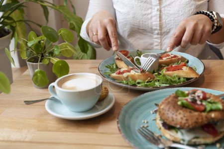 Téléchargez les photos : Femme mangeant un petit déjeuner végétarien sain au restaurant avec du pain et des légumes. Nourriture colorée sur une assiette sur une table avec les mains de la femme. Gros plan. - en image libre de droit