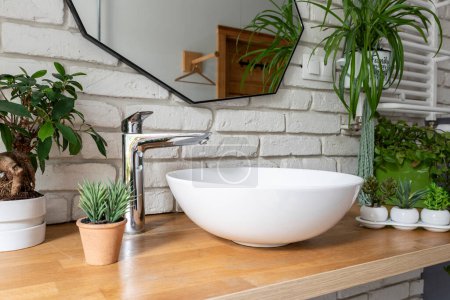 Téléchargez les photos : Intérieur de salle de bains dans un style industriel avec mur de briques blanches, miroir, plantes vertes, lavabo et comptoir en bois. Bain moderne. - en image libre de droit